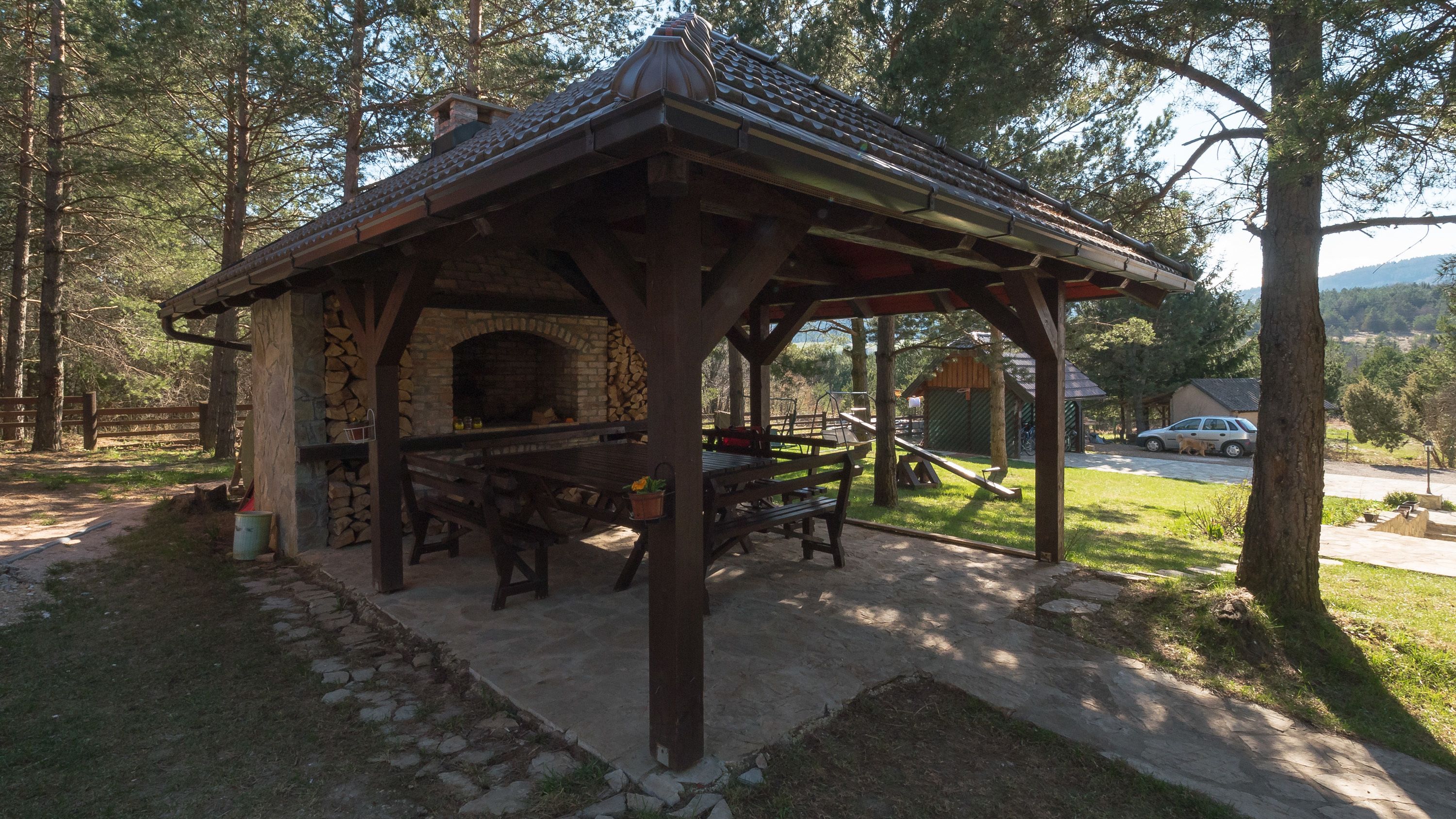A rustic outdoor pavilion with a stone fireplace, wooden benches, and a metal roof.