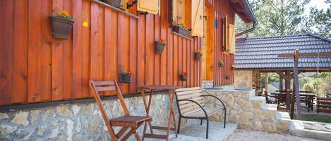 Una cabaña de madera con cimientos de piedra, muebles de madera y macetas en la pared exterior.