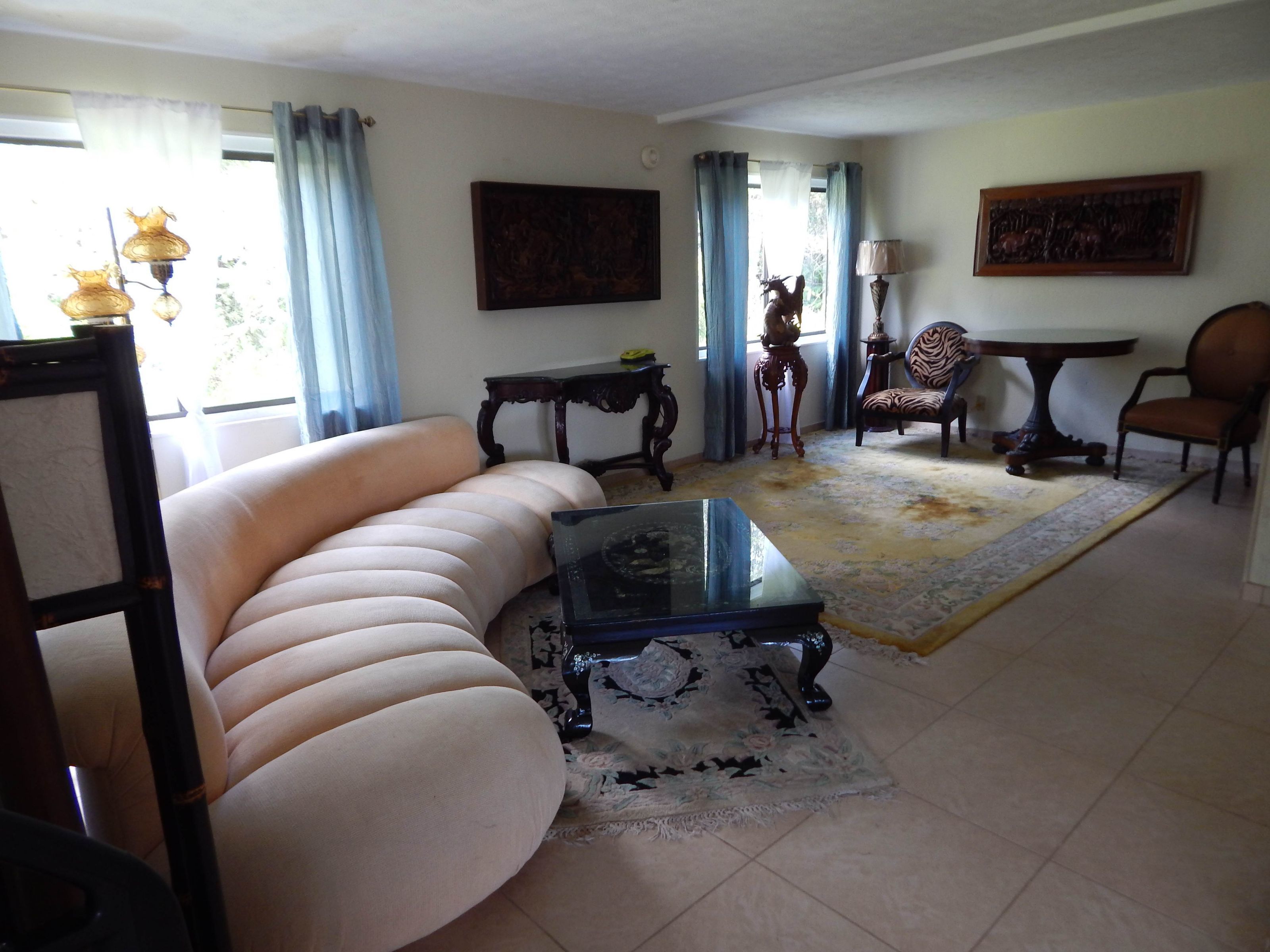 A living room with a beige sofa, a glass coffee table, a patterned rug, a zebra-striped chair, and a wooden table with a lamp.