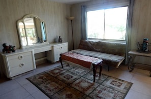 Une chambre à coucher avec un lit, une commode, un miroir, un banc et une fenêtre.