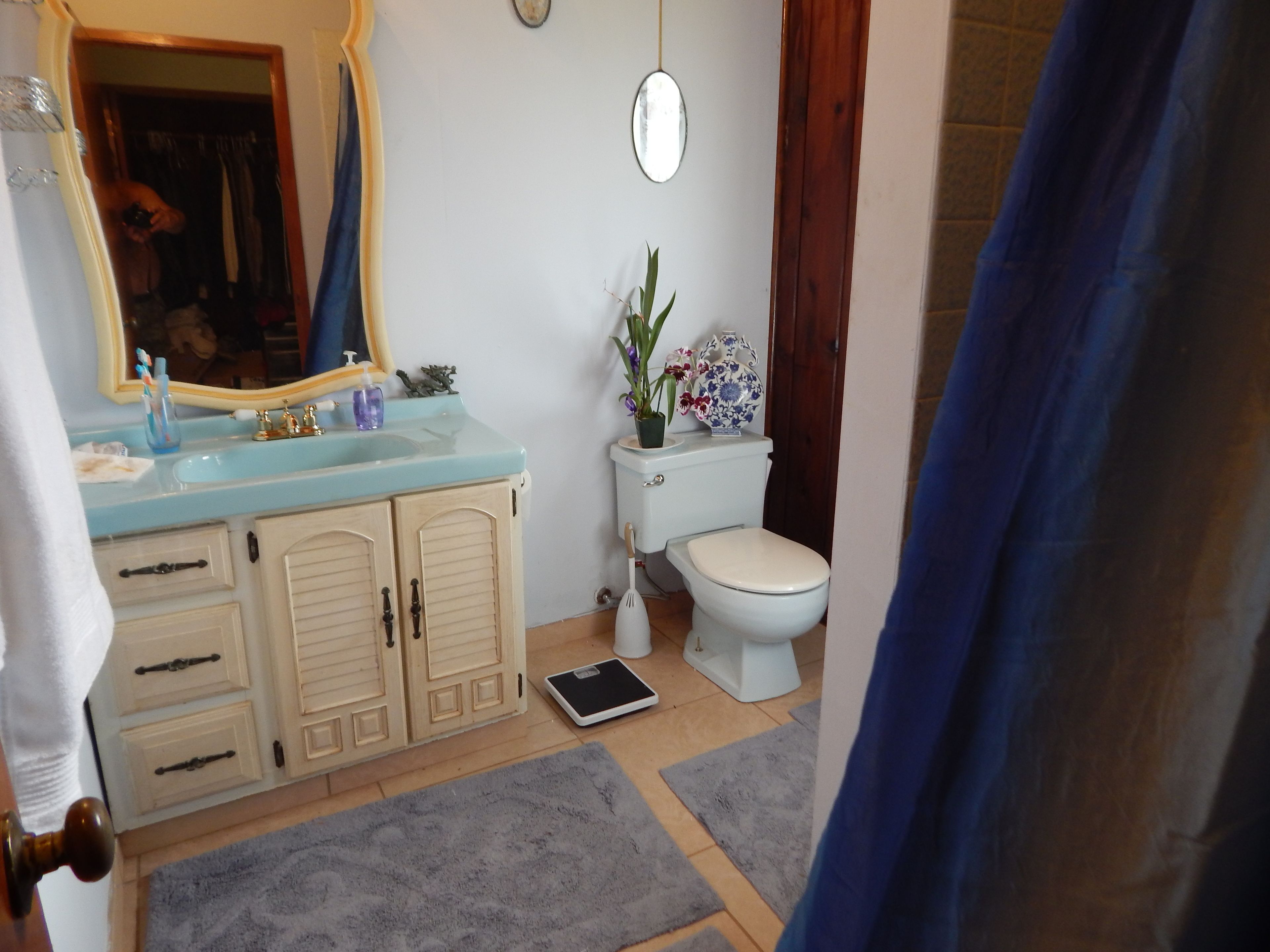 A bathroom with a sink, mirror, toilet, and a scale on the floor.