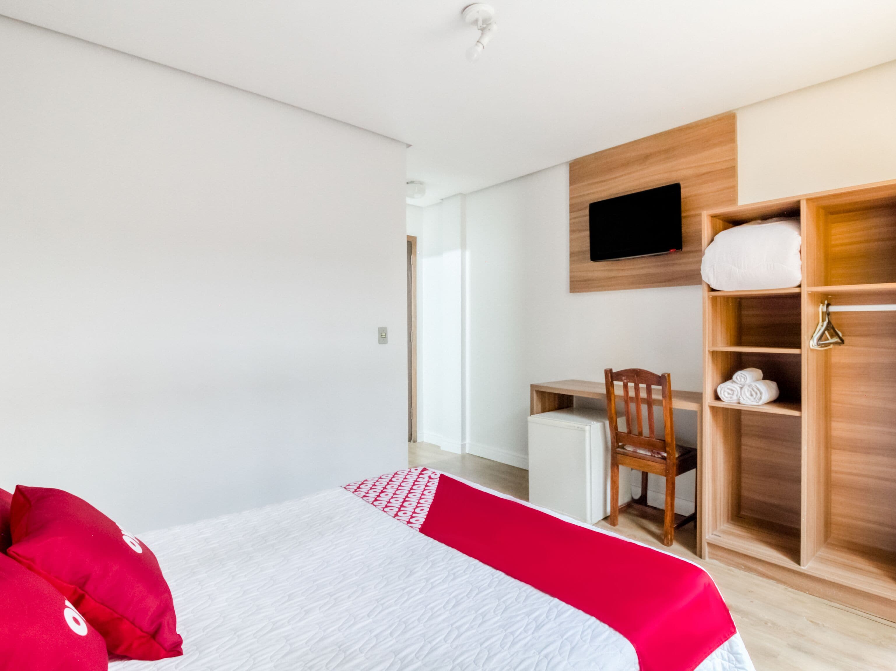 Una habitación de hotel moderna con una cama, un escritorio, una silla, un televisor y un armario.