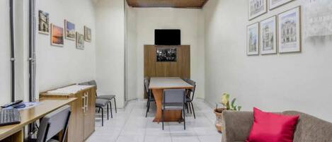 A room with a wooden ceiling, a dining table with chairs, a sofa with a red pillow, and framed pictures on the walls.