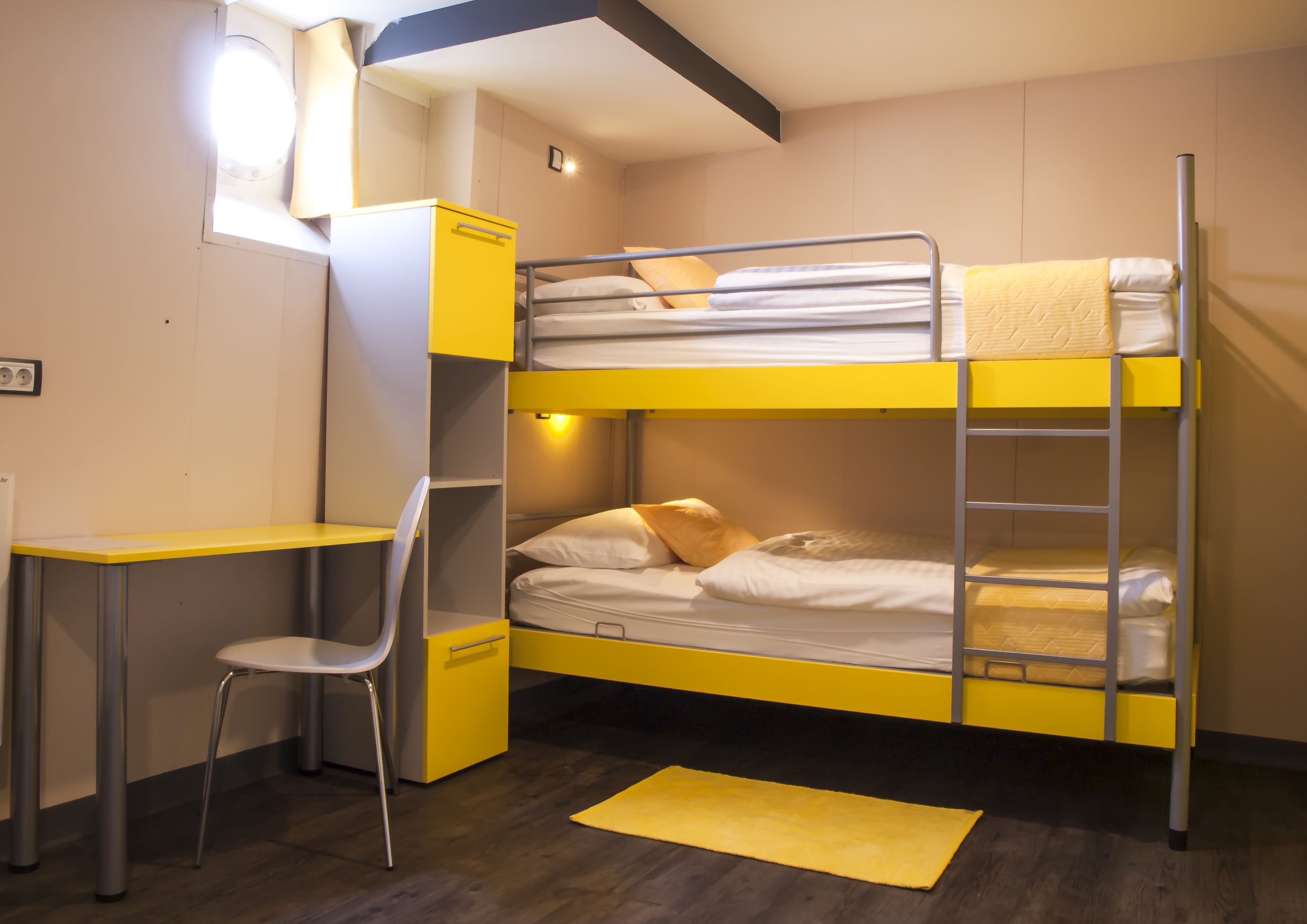 A bunk bed room with a desk and chair, a small window, and a yellow rug.