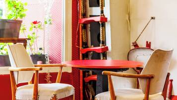 Una habitación con dos sillas de madera, una mesa roja, una escalera y una ventana con plantas.