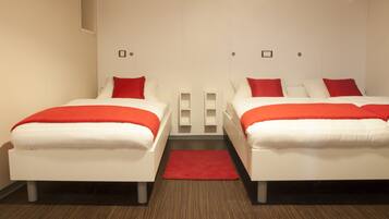 A hotel room with two beds, each with white bedding and red accents, a red rug, and a wooden floor.