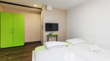 Una habitación de hotel con una cama, un armario verde, un televisor sobre un mueble bajo y una mesita.