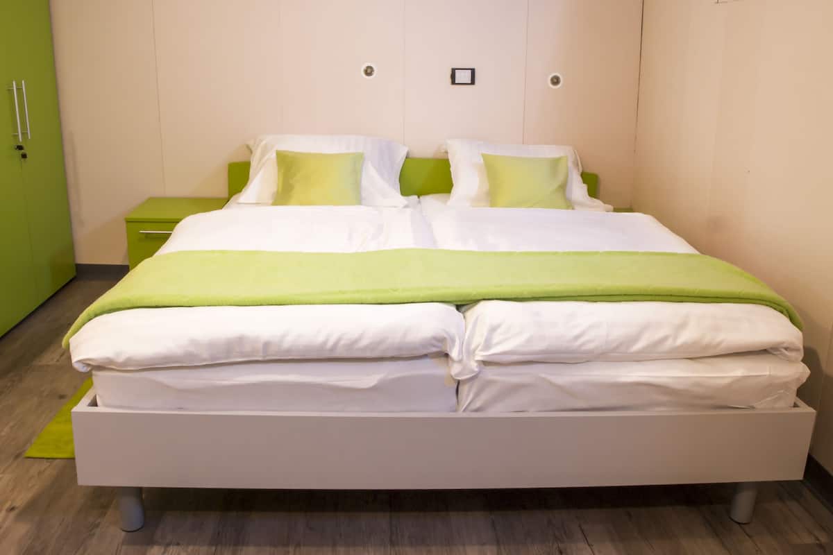 A neatly made bed with white and green bedding, a green nightstand, and a green wardrobe.