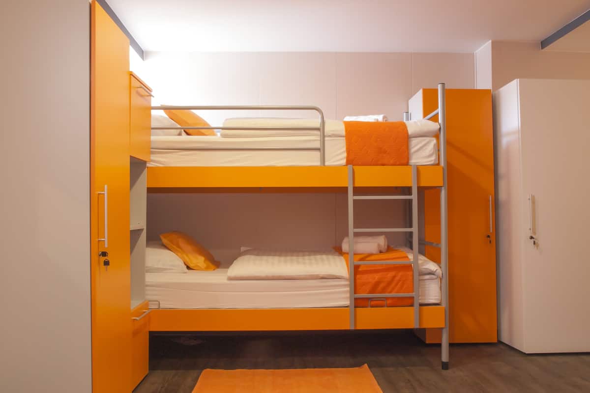 A bunk bed room with orange accents, a ladder, and a door.
