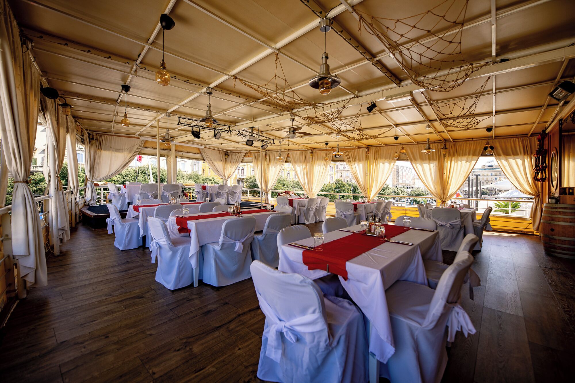 Amplia sala de comedor con mesas dispuestas para varios invitados, destacando un techo alto con vigas a la vista y lámparas colgantes.