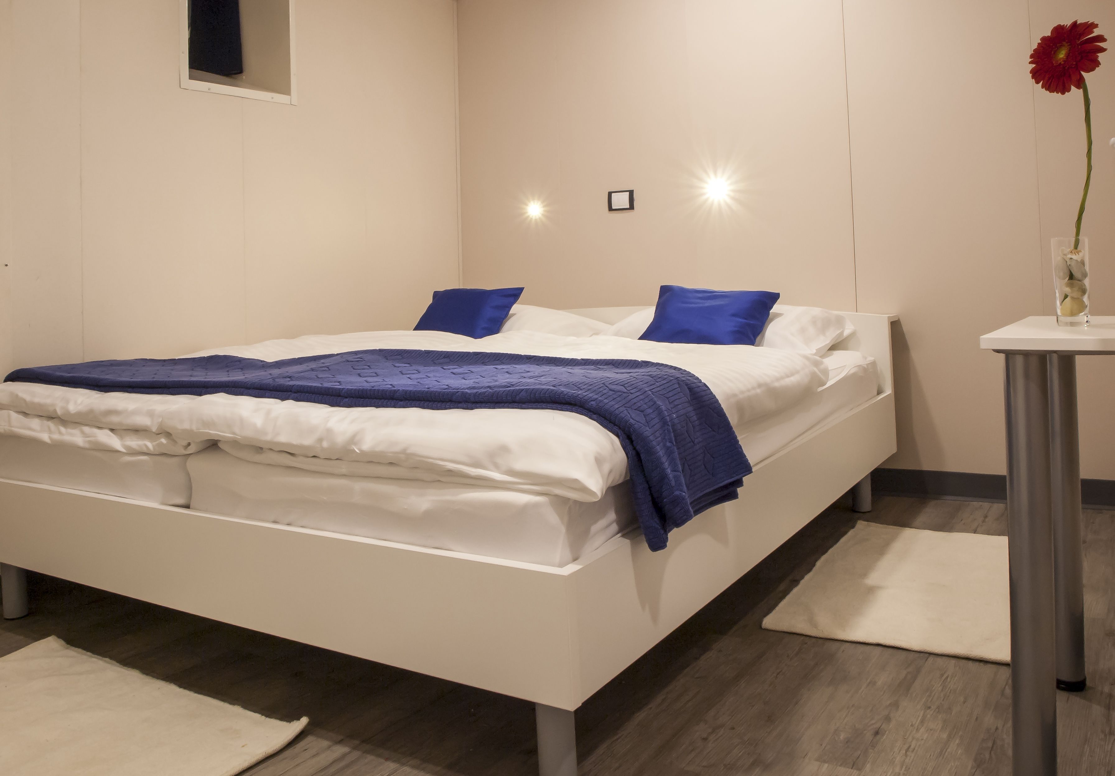 Un dormitorio moderno con una cama blanca, almohadas azules y una flor roja en un jarrón.