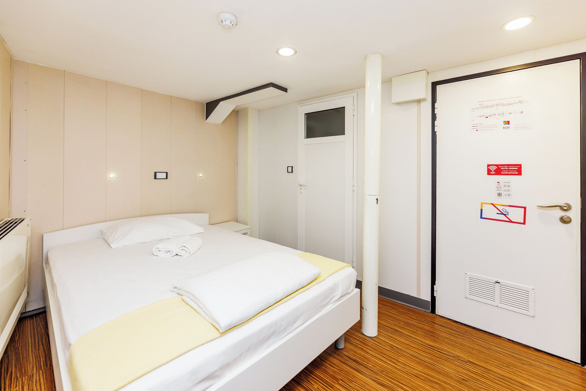 A hotel room with a bed, a bedside table, a wall-mounted TV, and a door with a sign.