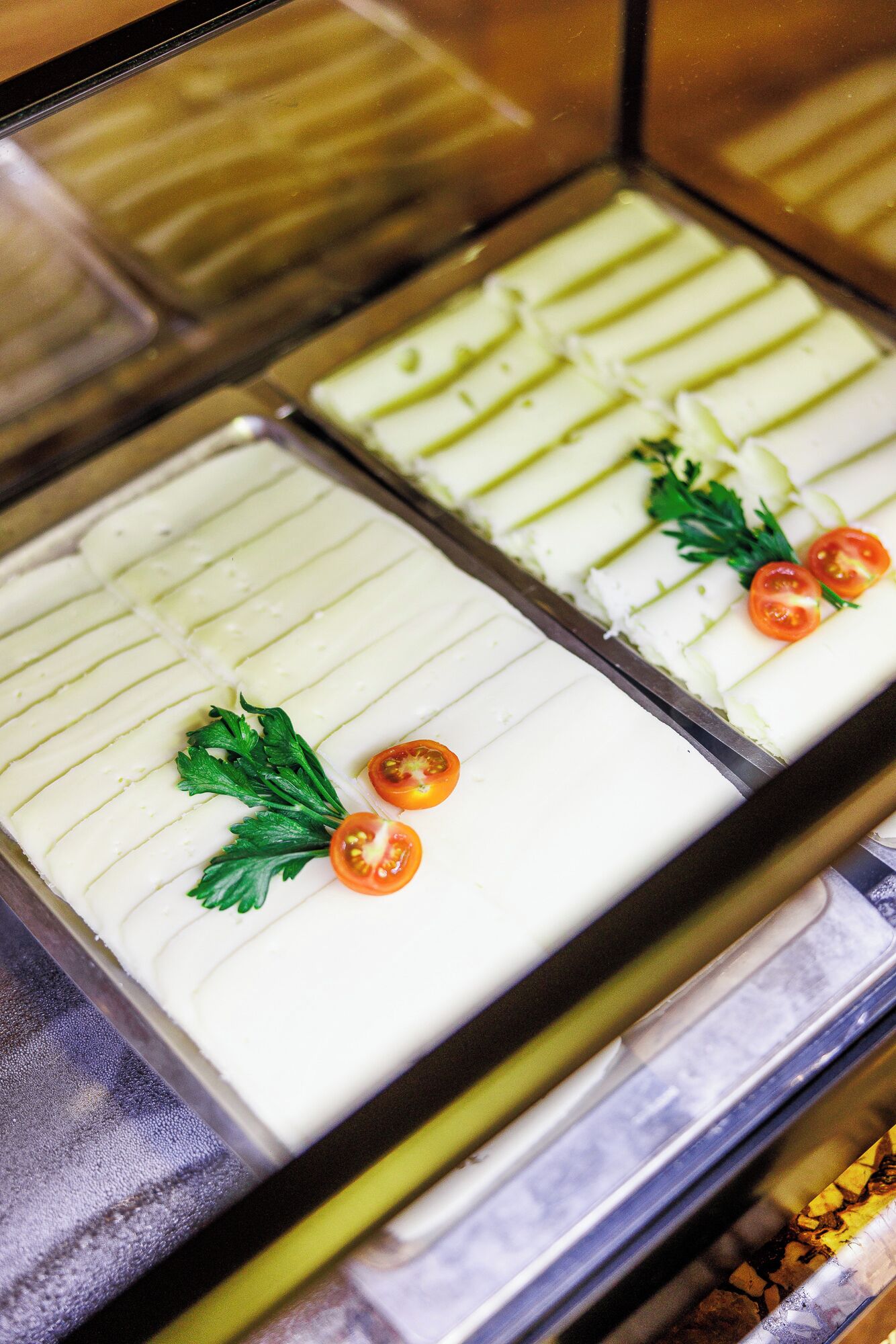 A display case with two sections of food, each with a green sauce and garnished with parsley and cherry tomatoes.