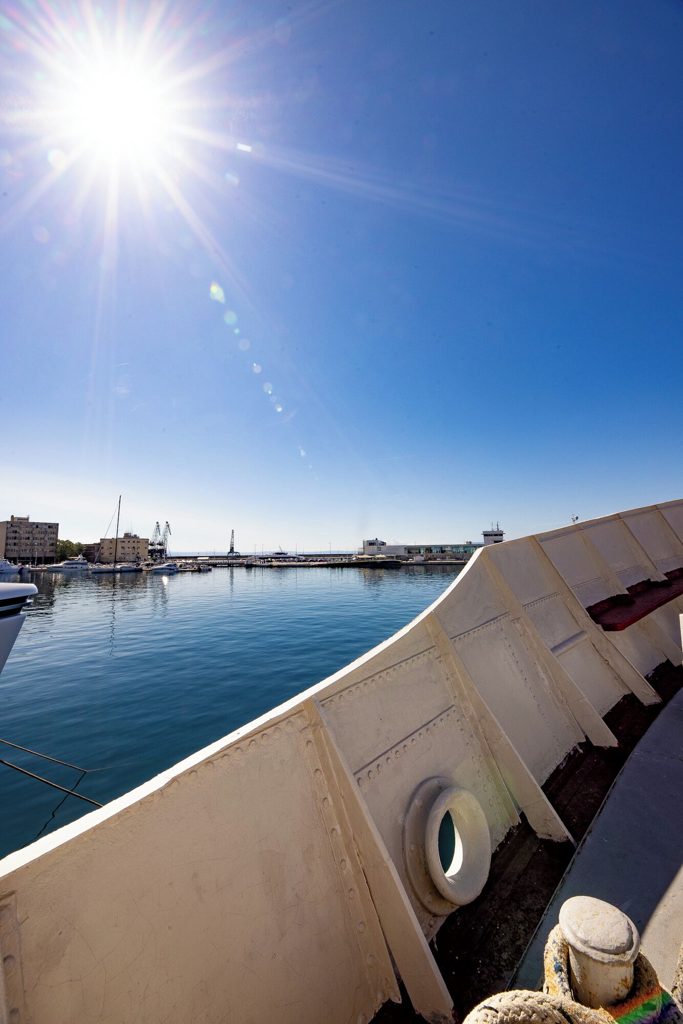 A marina with boats docked, a clear sky, and a sun shining.