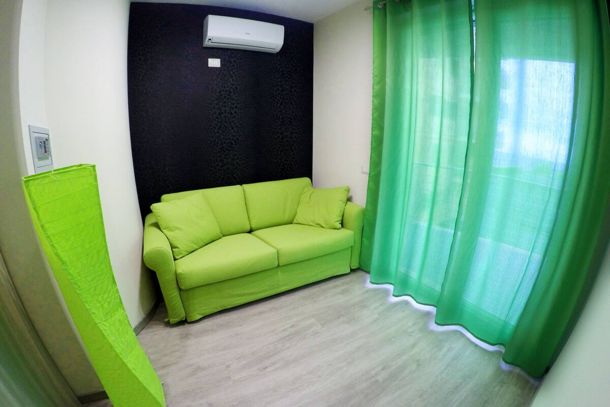 A room with a green sofa, a black textured wall, and a green curtain.