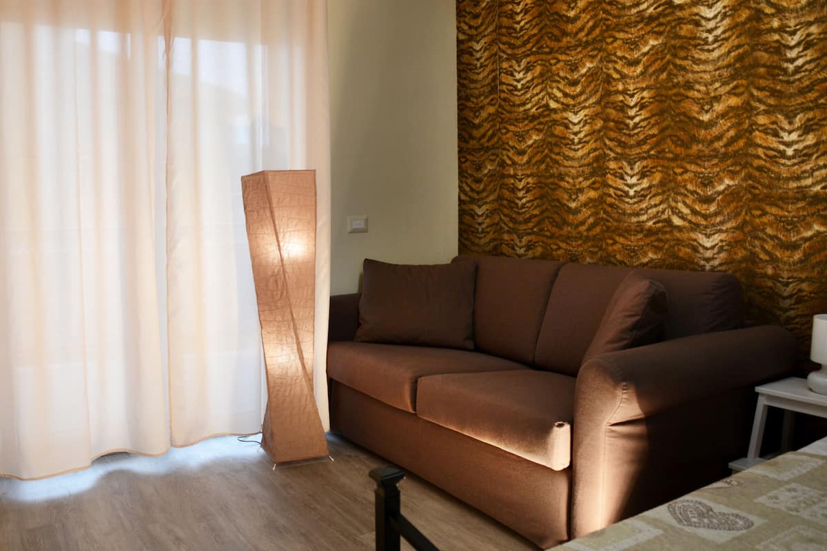 A living room with a brown sofa, a floor lamp, and a patterned wall.