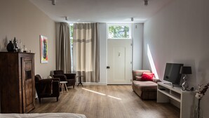 A hotel room with a wooden floor, a bed, a desk with a TV, a chair, a small table, and a cabinet. - Park43 (Haarlem)