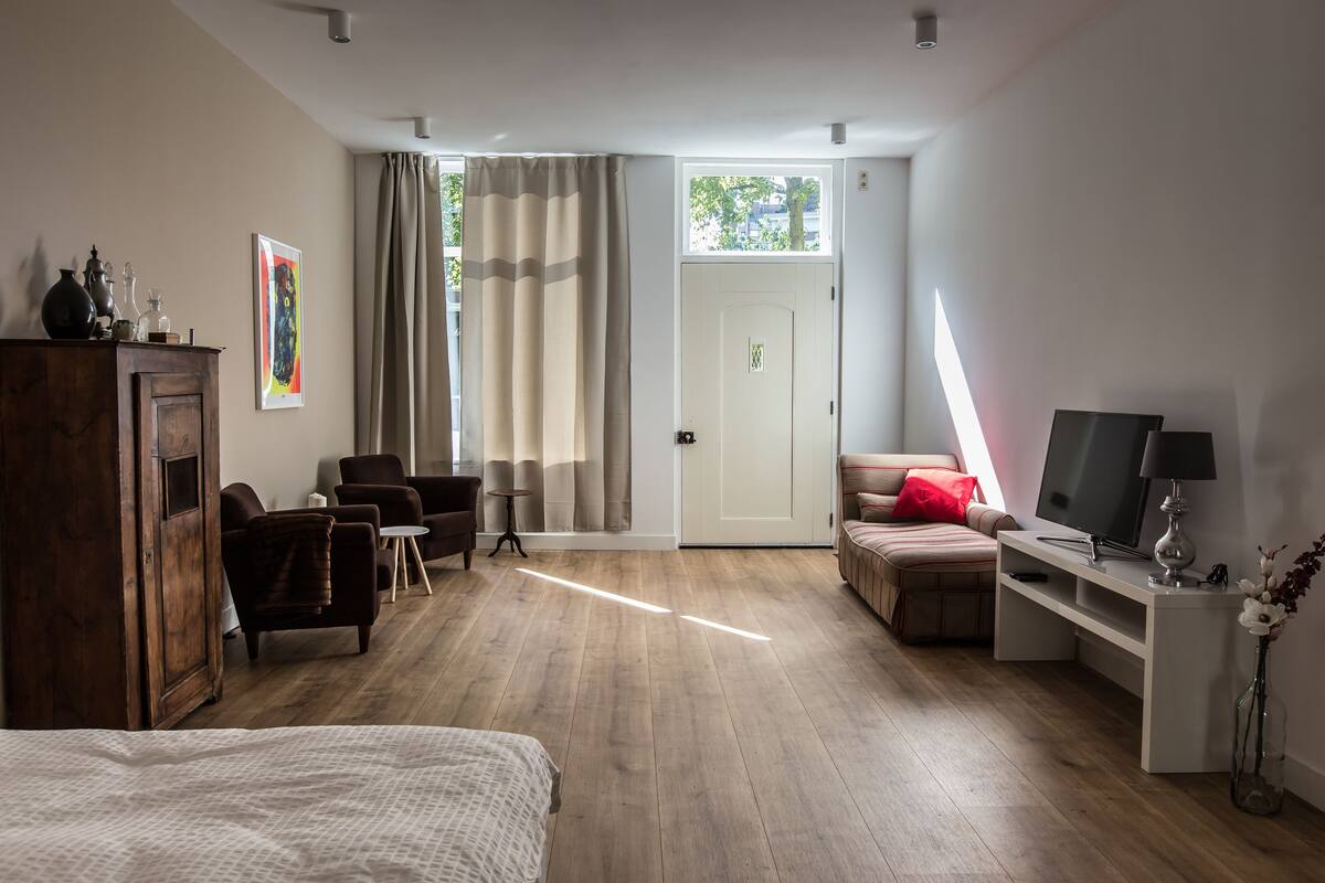 Une chambre d’hôtel avec un plancher en bois, un lit, un bureau avec une télévision, une chaise, une petite table et un placard.