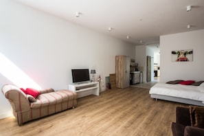 Habitación moderna y bien iluminada con sofá, televisor, cama y kitchenette.