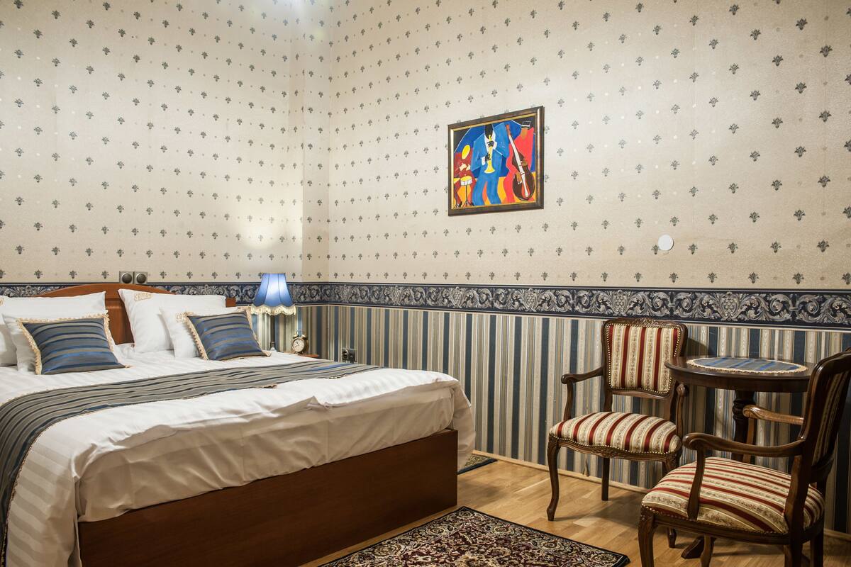 Un dormitorio con una cama grande, dos sillas, una mesita y una pared con diseño decorativo.