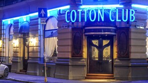 Um edifício com um letreiro de neon que diz "Cotton Club" e um símbolo de bicicleta indicando uma área que acolhe ciclistas.