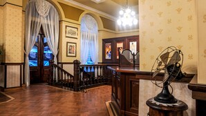 Um hall imponente com escada de madeira, teto ornamentado e decoração vintage, incluindo um leque e quadros emoldurados.