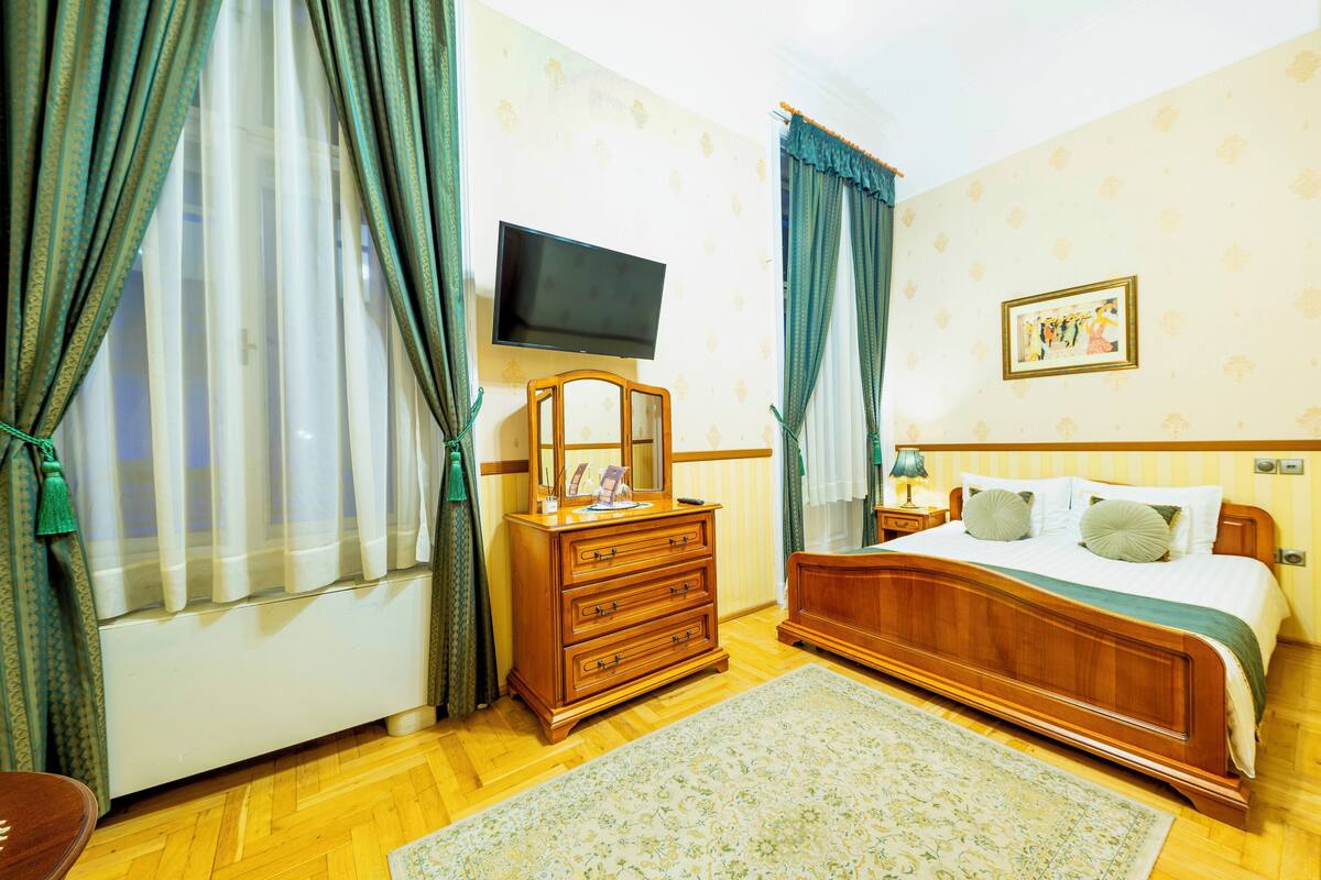 Un dormitorio con un aparador de madera, un televisor montado en la pared, una cama con almohadas y un cuadro enmarcado.