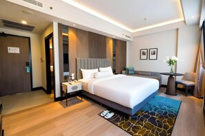 Una habitación de hotel moderna con una cama grande, una mesita de noche y un pequeño rincón de estar con una mesa y una silla.