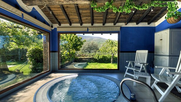 Un cuarto de spa con hidromasaje, dos sillas blancas, vistas a un jardín y techo de madera.