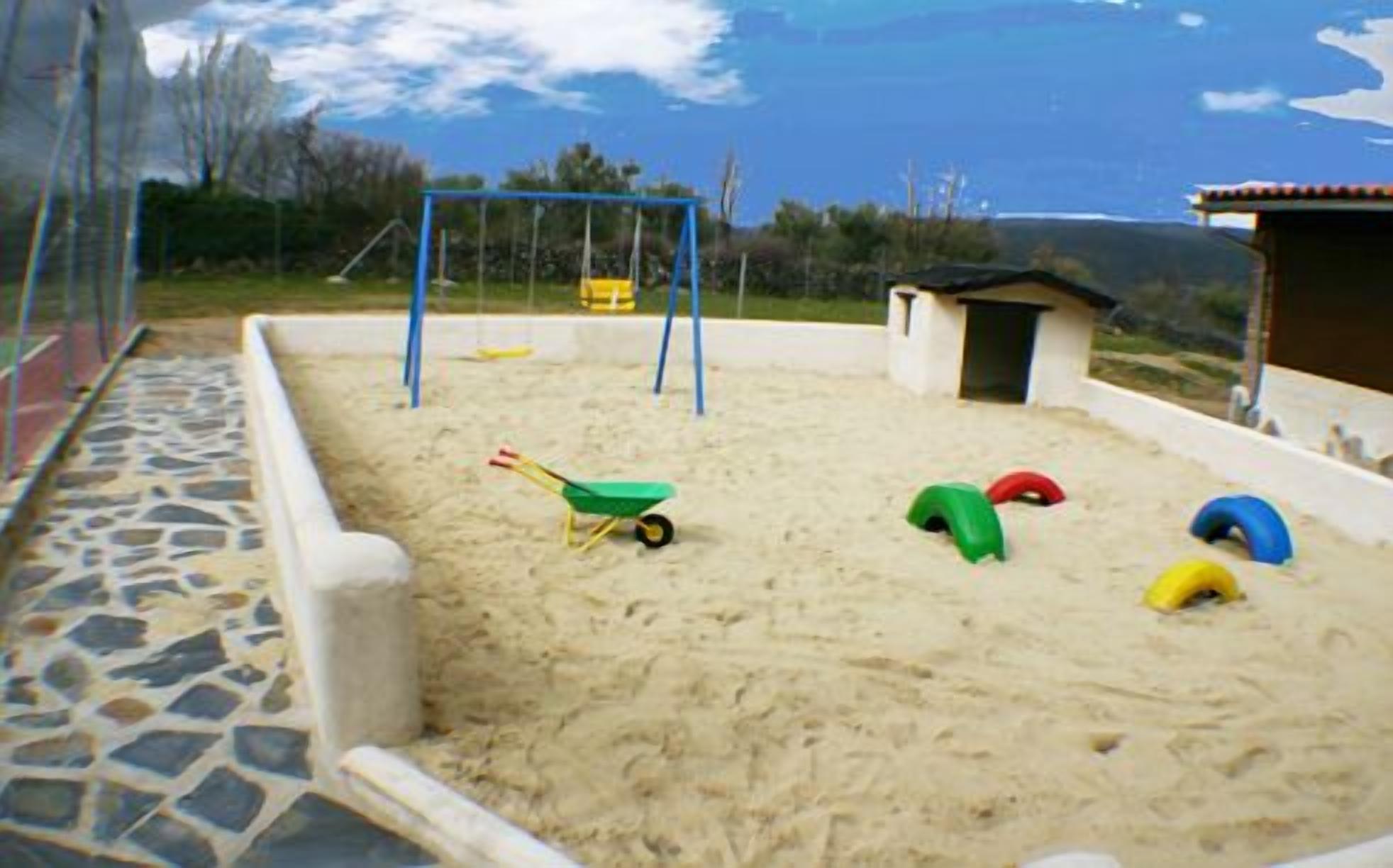 A sandy play area with a swing set, a small shed, and a wheelbarrow.