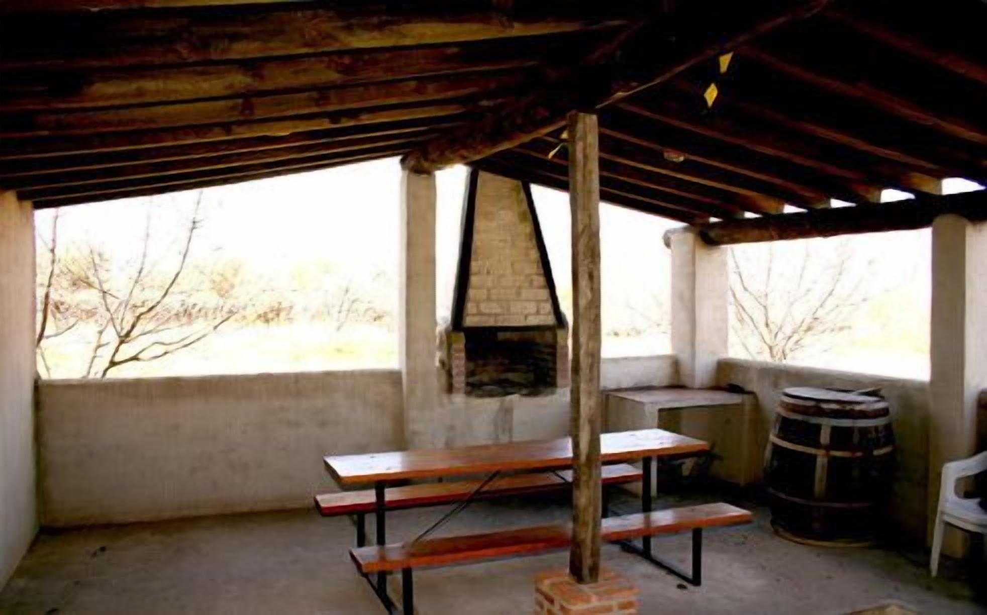 Un área de comedor al aire libre rústica, con chimenea de ladrillo, bancos de madera y un barril.