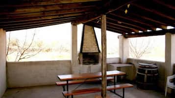 Un área de comedor al aire libre rústica, con chimenea de ladrillo, bancos de madera y un barril.