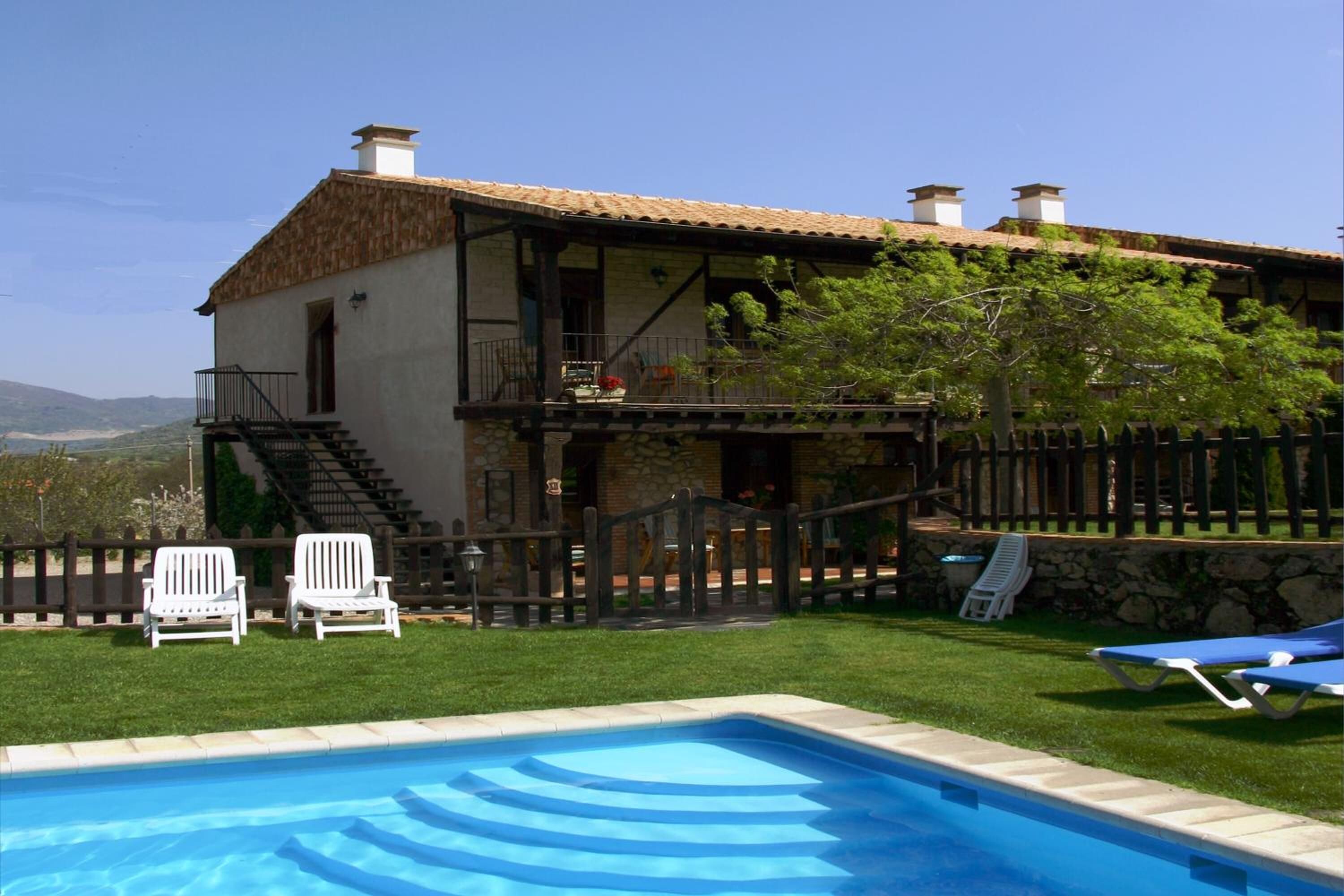 A two-story house with a swimming pool, a wooden deck, and a stone wall.