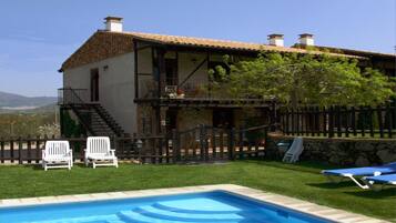 A two-story house with a swimming pool, a wooden deck, and a stone wall.
