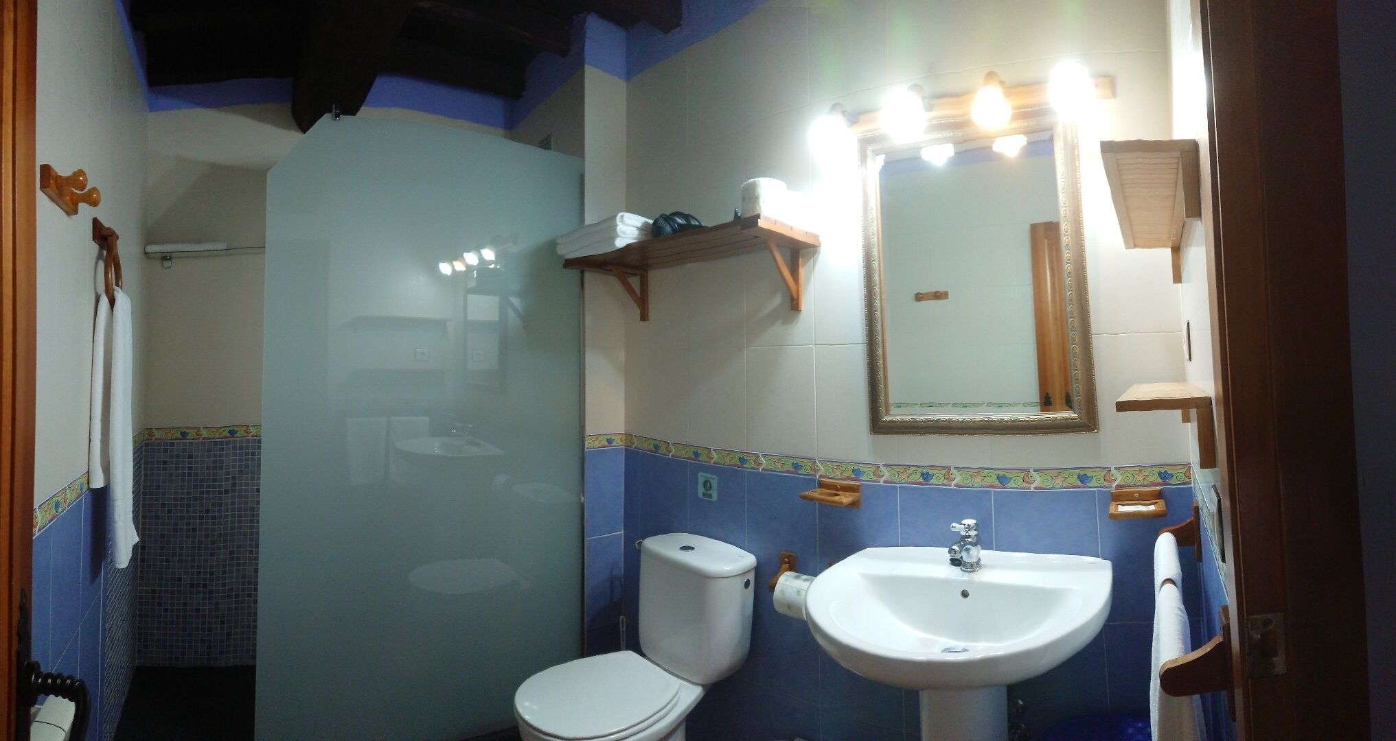 Un baño con inodoro, lavabo y espejo. Cuenta con un perchero y un estante con artículos de aseo.