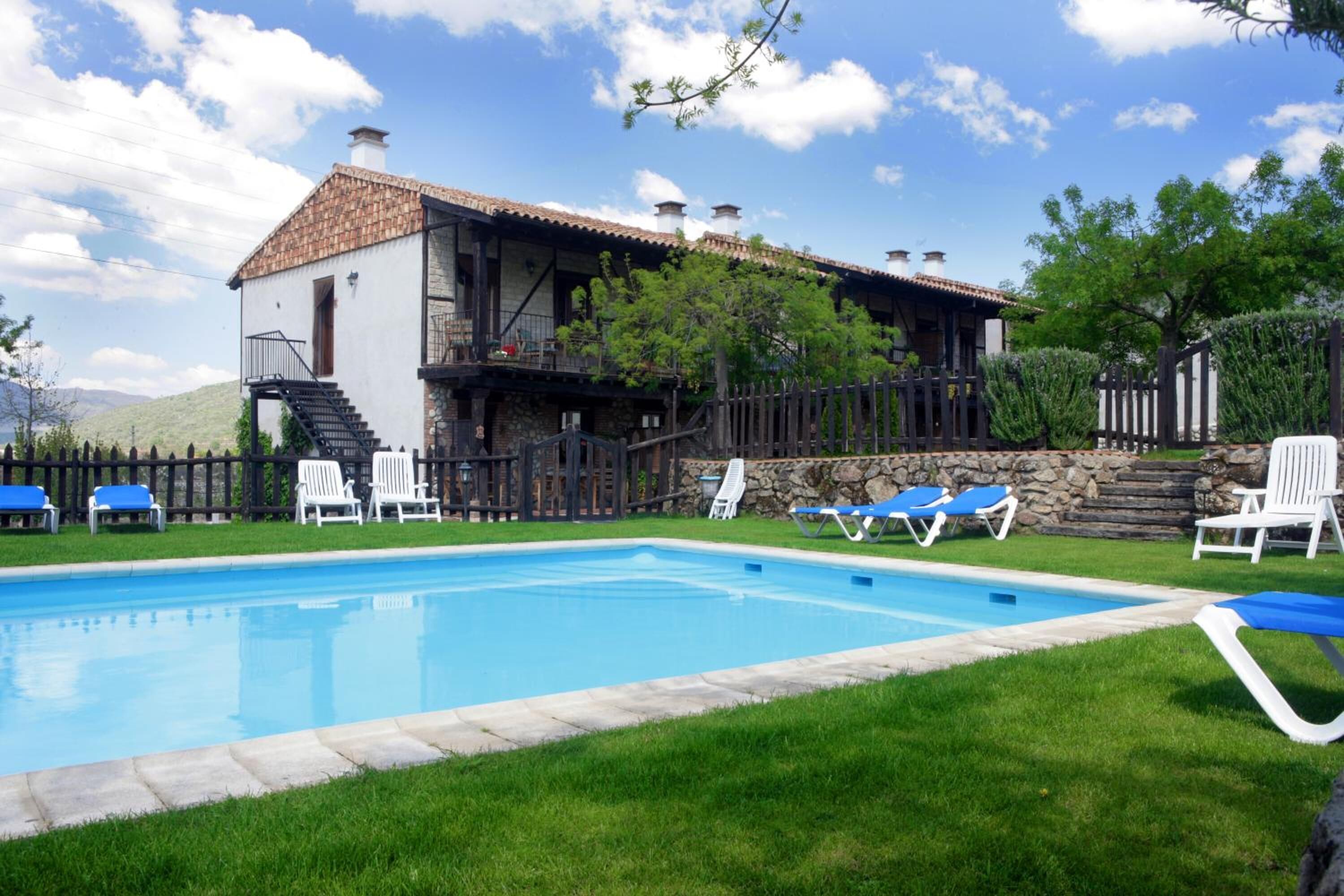 Una piscina con sillas de descanso azules y blancas, un muro de piedra y un edificio con techo de tejas.