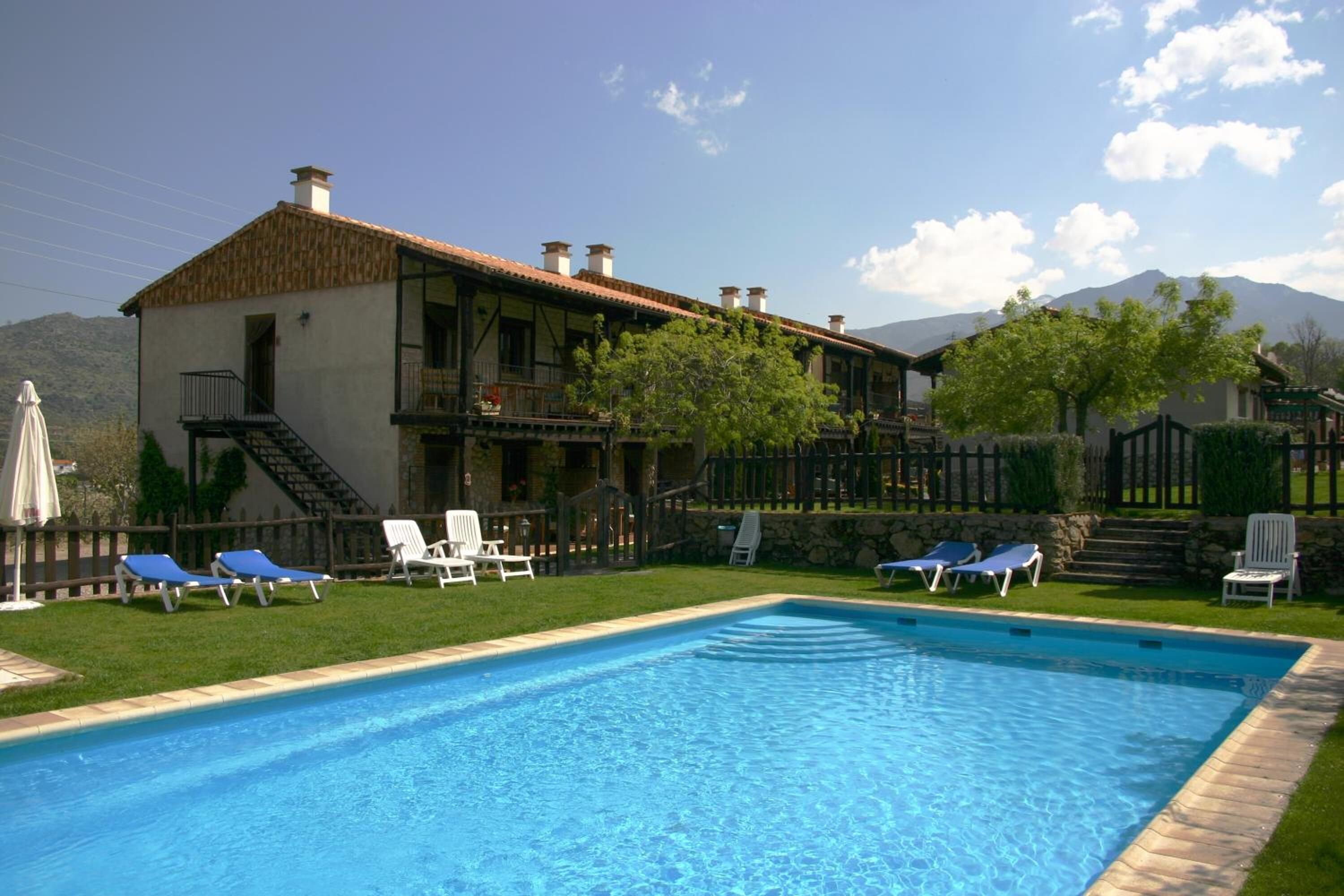 A pool with lounge chairs, a building with a balcony, and a mountain in the background.