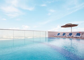Une piscine à débordement située sur le toit, avec une eau d’un bleu cristallin, une vue sur la ville et des chaises longues dotées de parasols.