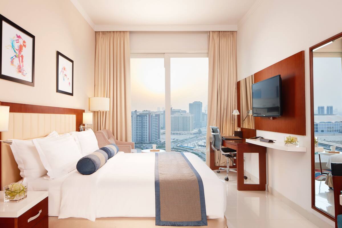 A hotel room with a large bed, a desk, a TV, and a view of the cityscape.