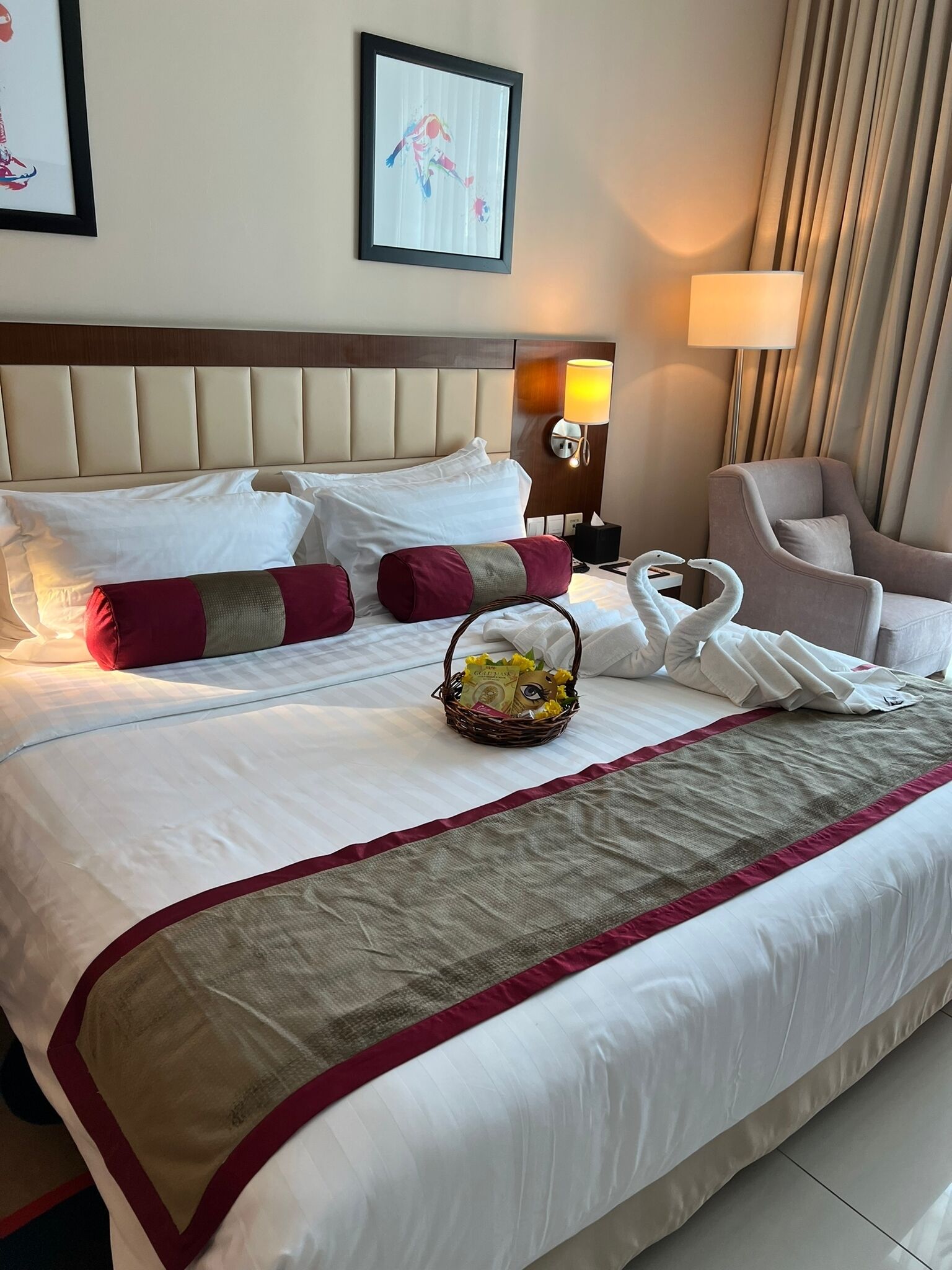 Ein Hotelzimmer mit einem großen Bett, einem Kopfteil, einer Lampe, einem Sessel und einem gerahmten Bild an der Wand.