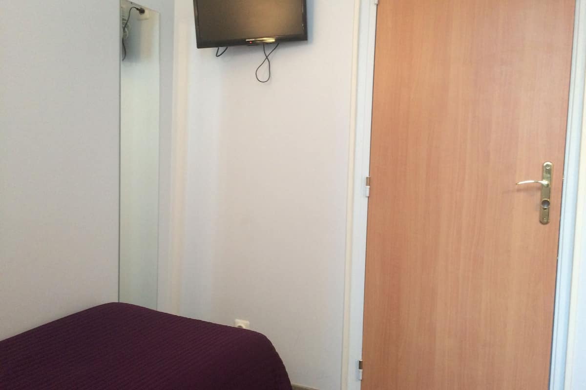 Una habitación con una cama, una puerta de madera y un televisor montado.