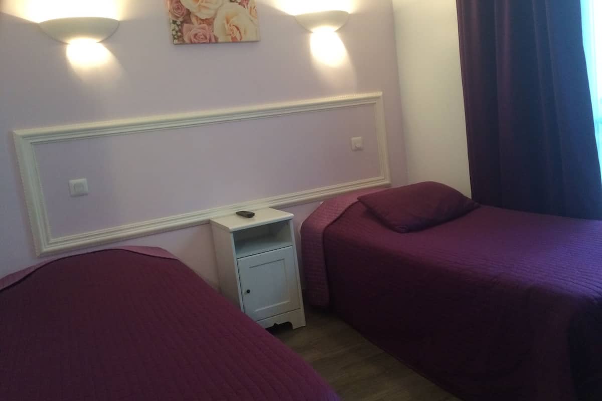 Una habitación de hotel con dos camas, una mesita de noche y una lámpara fijada a la pared.