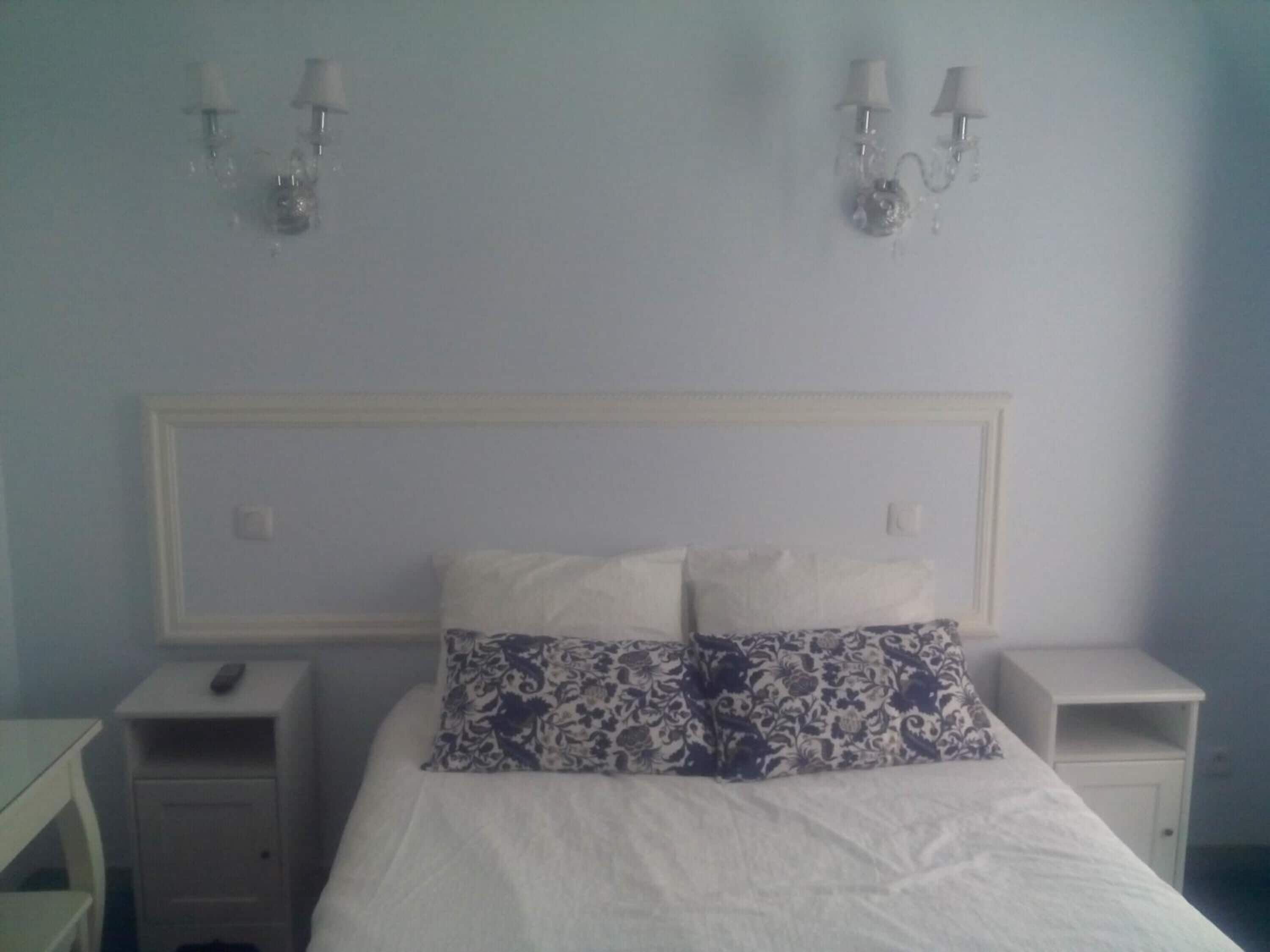 A bedroom with a bed, two bedside tables, and wall-mounted lamps.