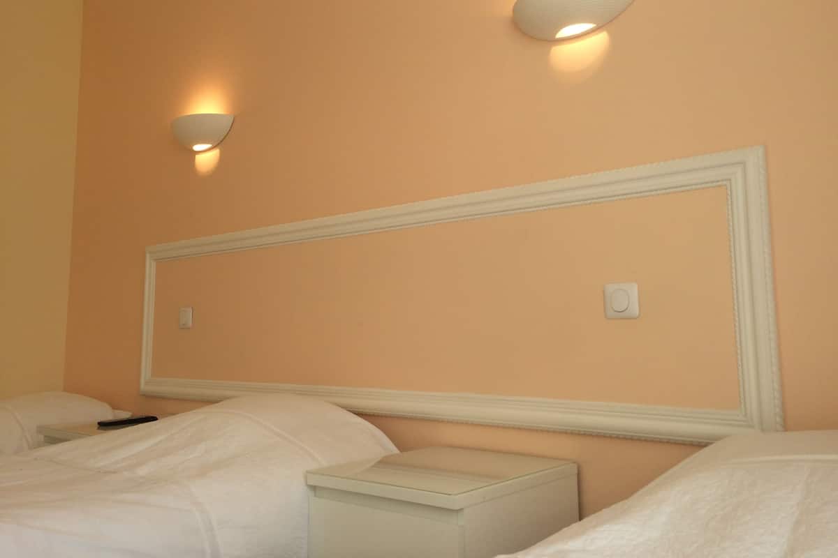 Habitación de hotel con un espejo grande sobre la cama, una mesita de noche y dos lámparas fijadas a la pared.