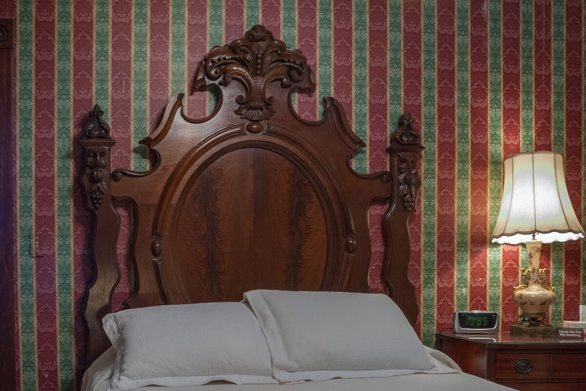 A neatly made bed with a wooden headboard, a bedside table with a lamp, and a wall with striped wallpaper.