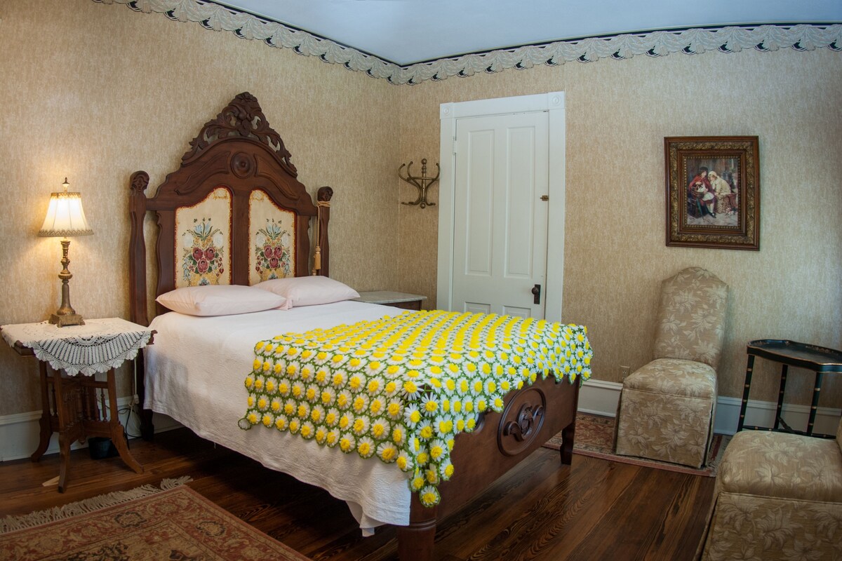 A bedroom with a wooden bed, a white door, a chair, and a lamp.