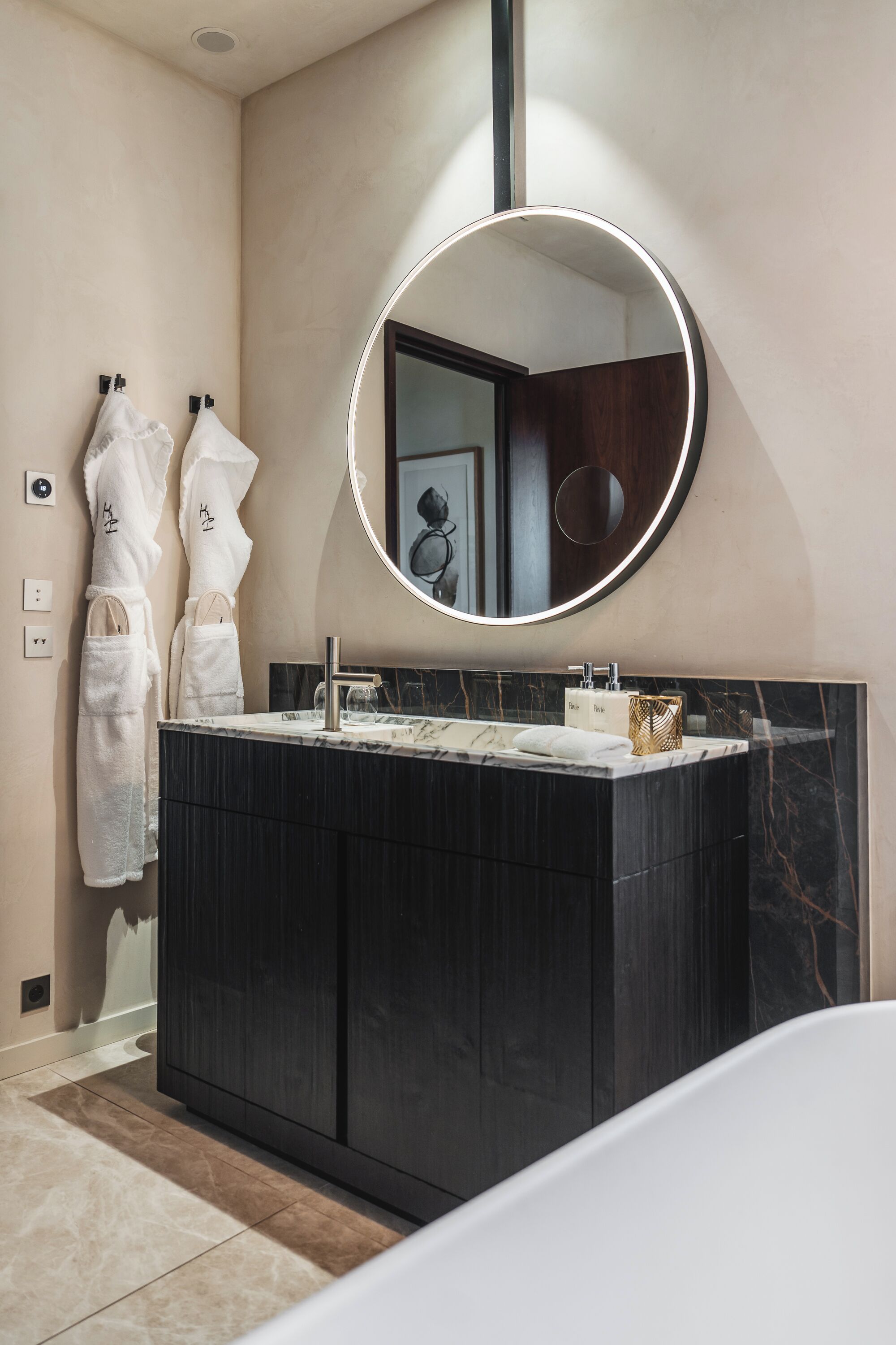 A modern bathroom with a dark vanity, a round mirror, and two white towels hanging on hooks.