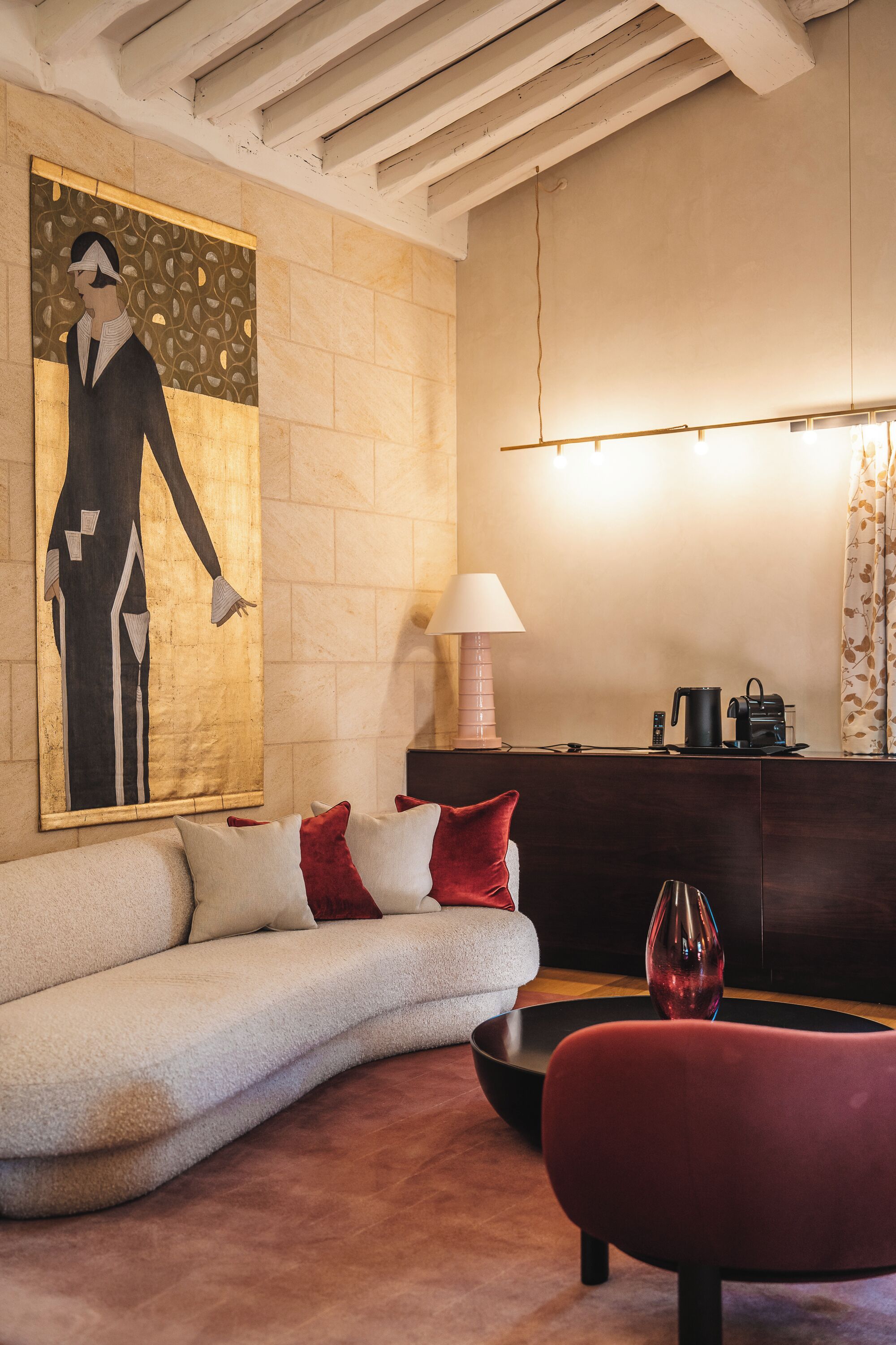 A modern living room with a sofa, a red chair, a coffee table, a lamp, and a painting on the wall.