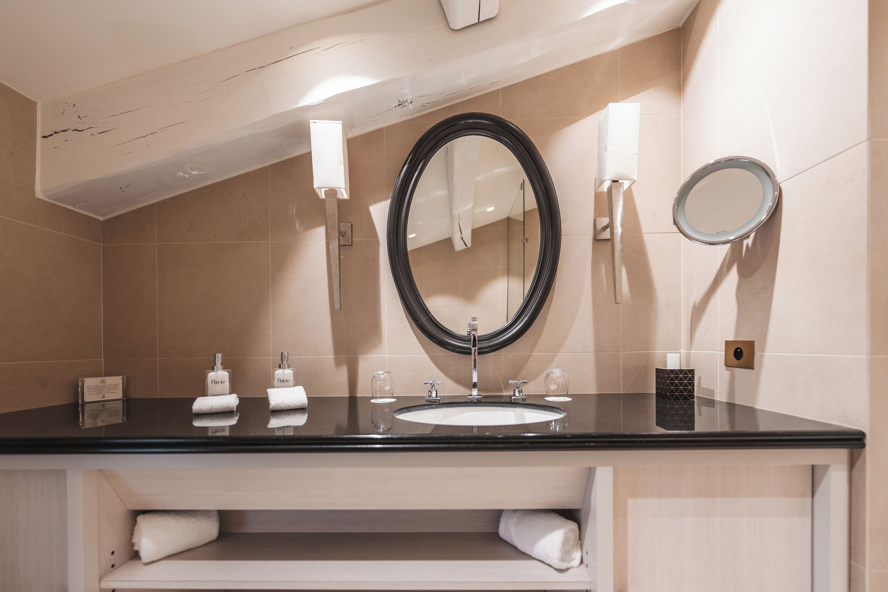 A modern bathroom with a black countertop, a white sink, a large mirror, and two towel dispensers.