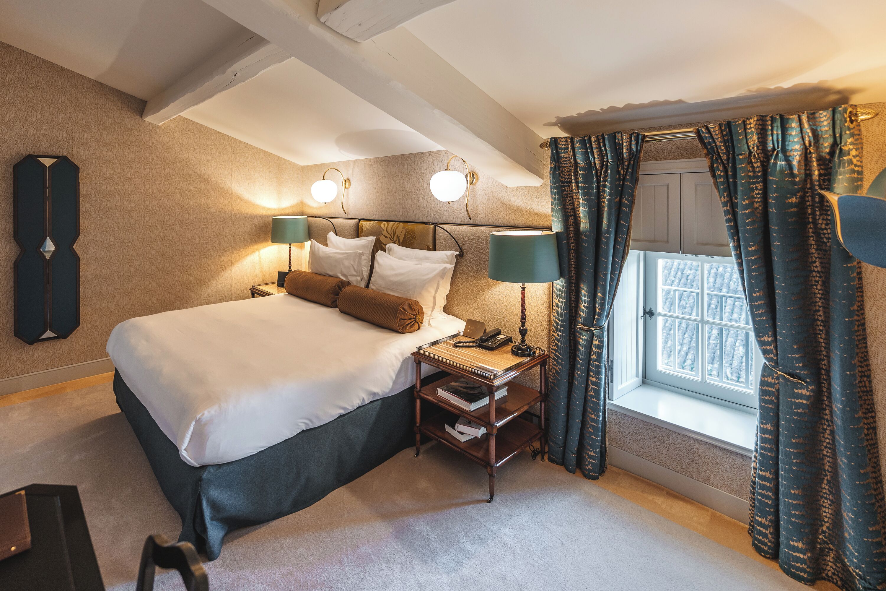 A neatly arranged bedroom with a large bed, bedside lamps, a nightstand, and a window with curtains.